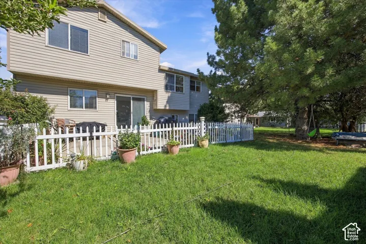 Expansive lawn area with a white picket fence, large mature tree, and a concrete patio