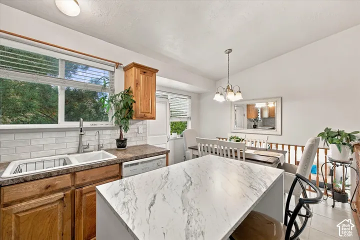 Kitchen featuring a dual basin sink, light wood-finish cabinetry, a white subway tile backsplash, and a breakfast bar with a light-toned countertop