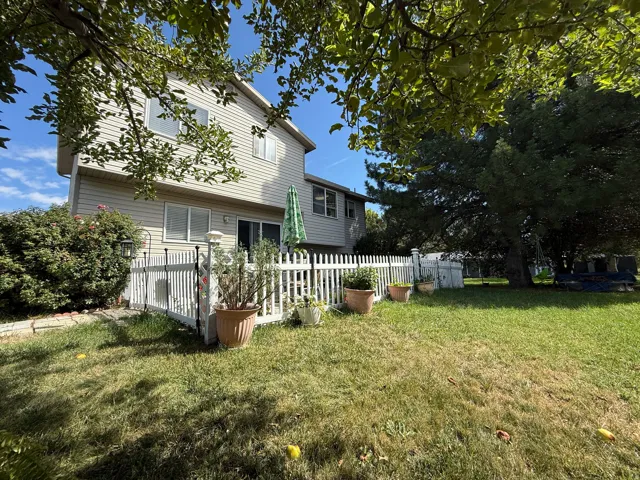 Expansive backyard featuring a manicured lawn, white picket fence, mature trees, and a two-story residence with siding exterior