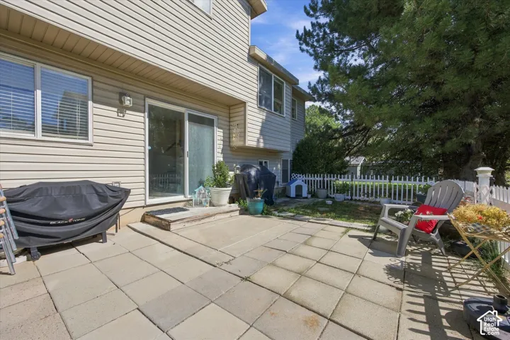Expansive paver patio with a sliding glass door entry to the residence, complemented by a white picket fence and mature landscaping