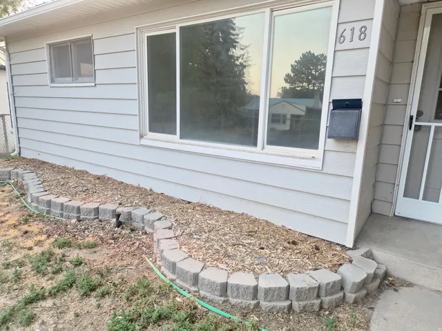 Light-colored horizontal siding, large front window, address numbers 618, wall-mounted mailbox, and a concrete paver retaining wall