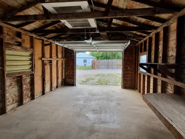 Concrete flooring, exposed wood beam ceiling, built-in shelving, and garage door opener