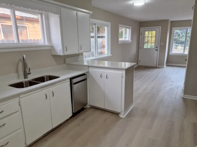 White cabinetry, stainless steel sink, contemporary faucet, light wood-finish flooring, and a stainless steel dishwasher