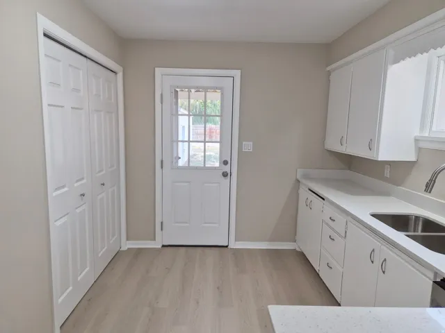 Wood-finish flooring with white baseboards, white paneled bifold closet doors, white paneled rear exterior door with window, white cabinetry, and white countertops
