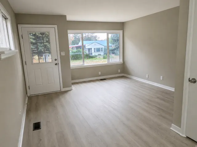 Light wood-finish flooring, neutral wall tones, white trim, multiple windows, and a door with an integrated glass panel