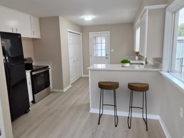 White cabinetry, stainless steel range, light-toned wood-finish flooring, white countertop, and bi-fold closet doors