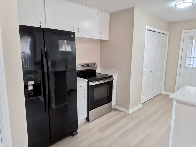 Light wood-finish flooring, white cabinetry, stainless steel range, and a white countertop