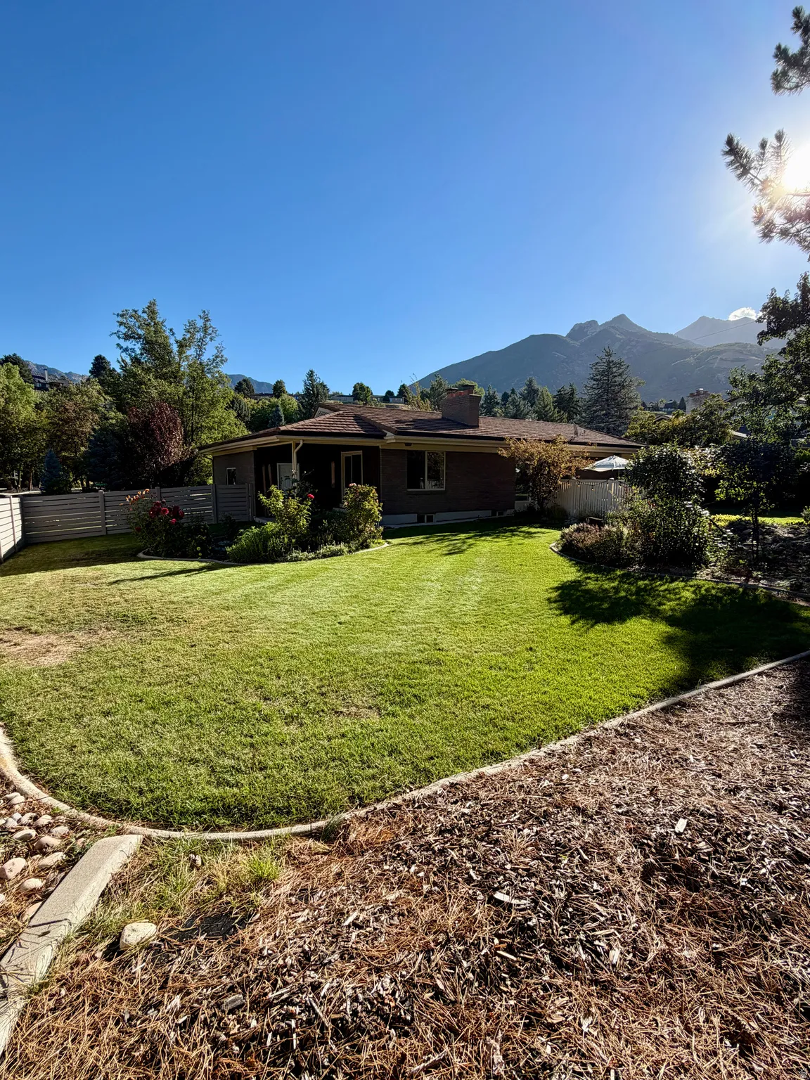 Expansive backyard featuring a manicured lawn, mature landscaping, and mountain backdrop