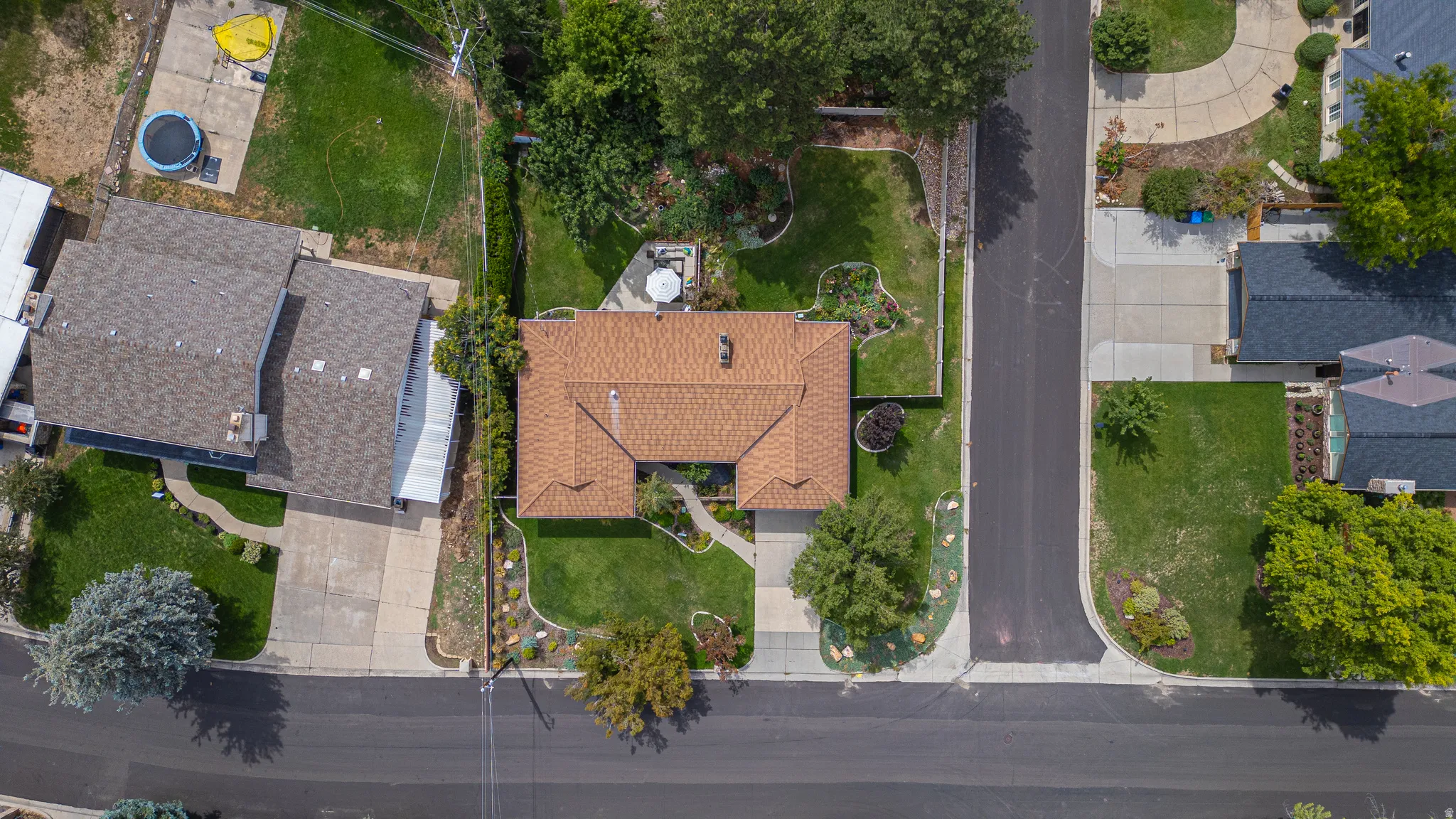 Single-story residence featuring a brown shingle roof, paved driveway, and landscaped front yard with mature trees