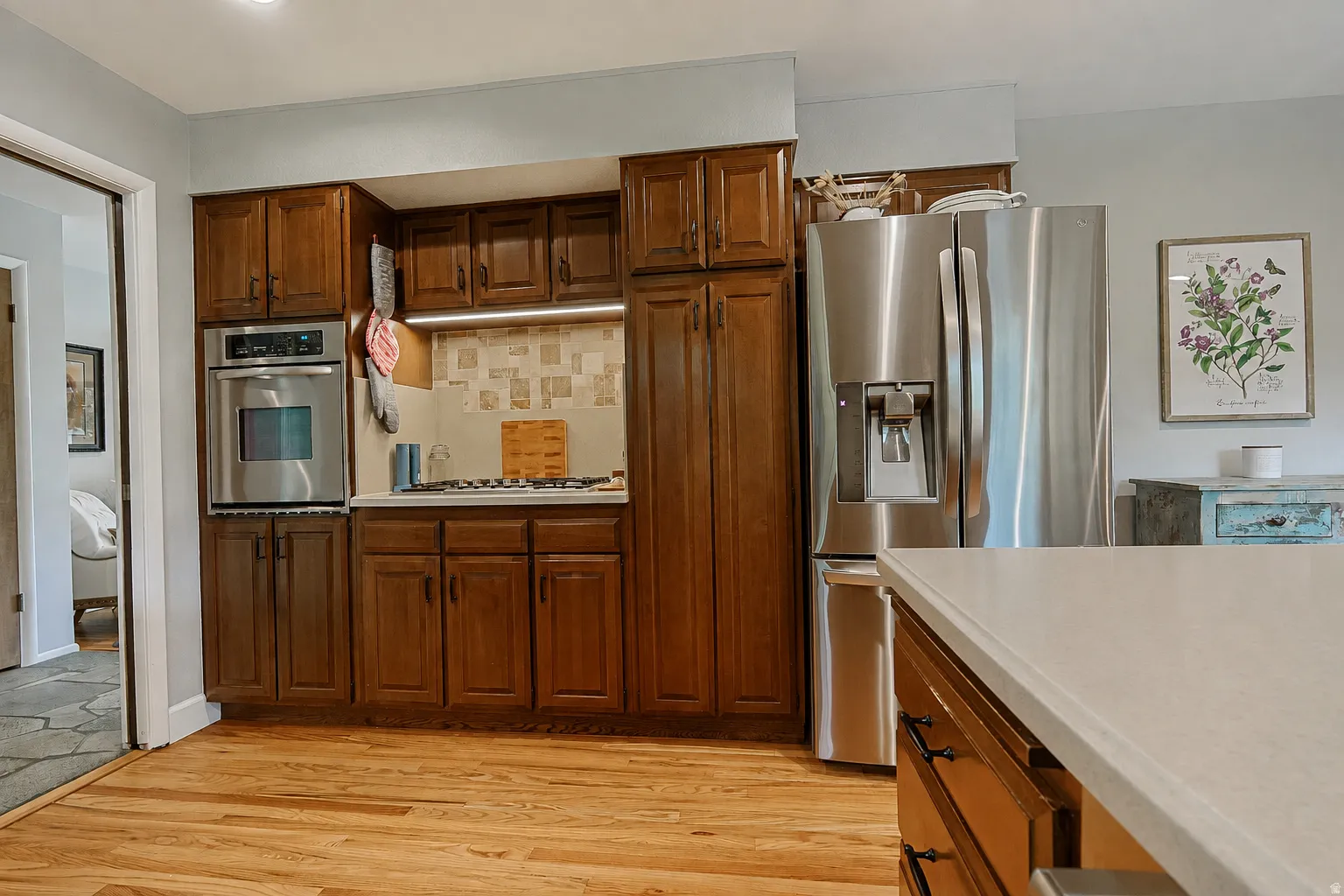 Wood-finish flooring, built-in stainless steel oven, gas cooktop, wood cabinetry, and stainless steel French door refrigerator