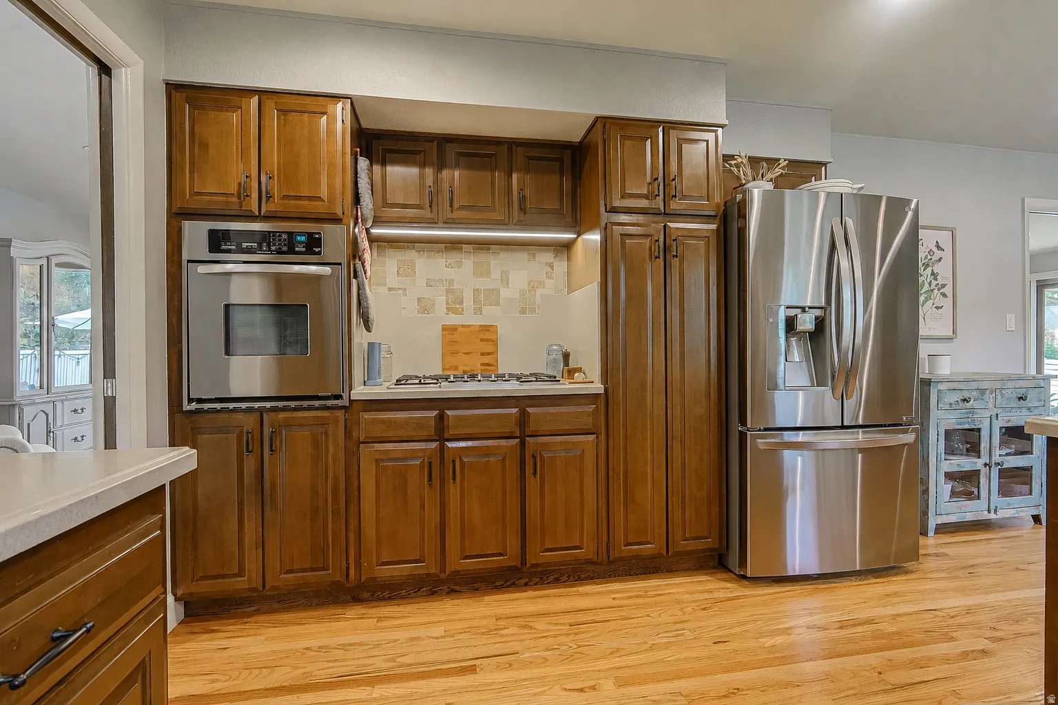 Hardwood flooring, stainless steel built-in oven, stainless steel refrigerator, gas cooktop, and wood-finish cabinetry