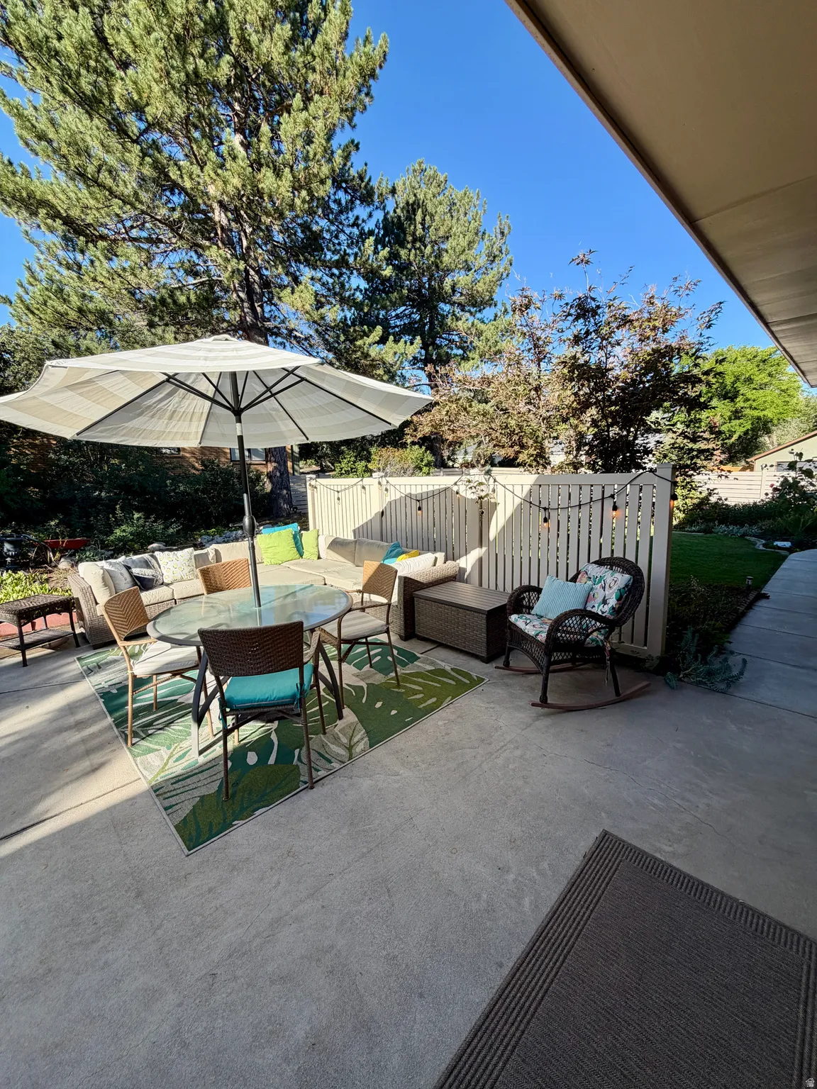 Concrete patio with white picket fencing, string lighting, and mature trees