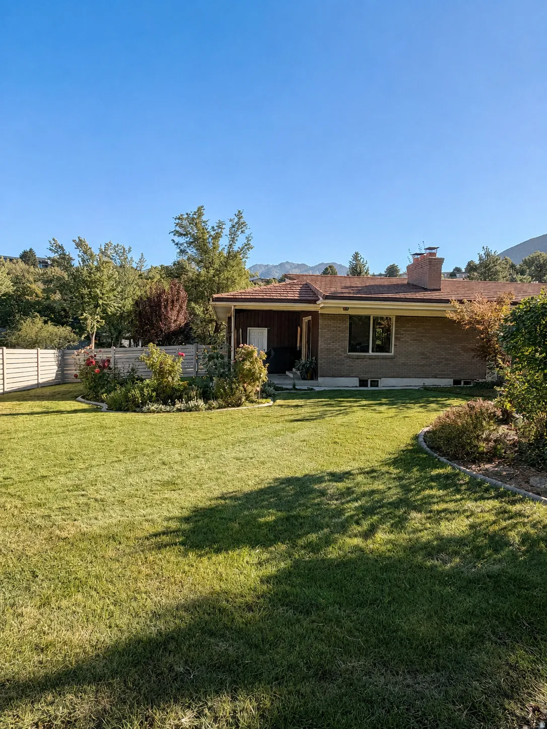 Expansive lawn with mature landscaping, a brick exterior, and a covered patio