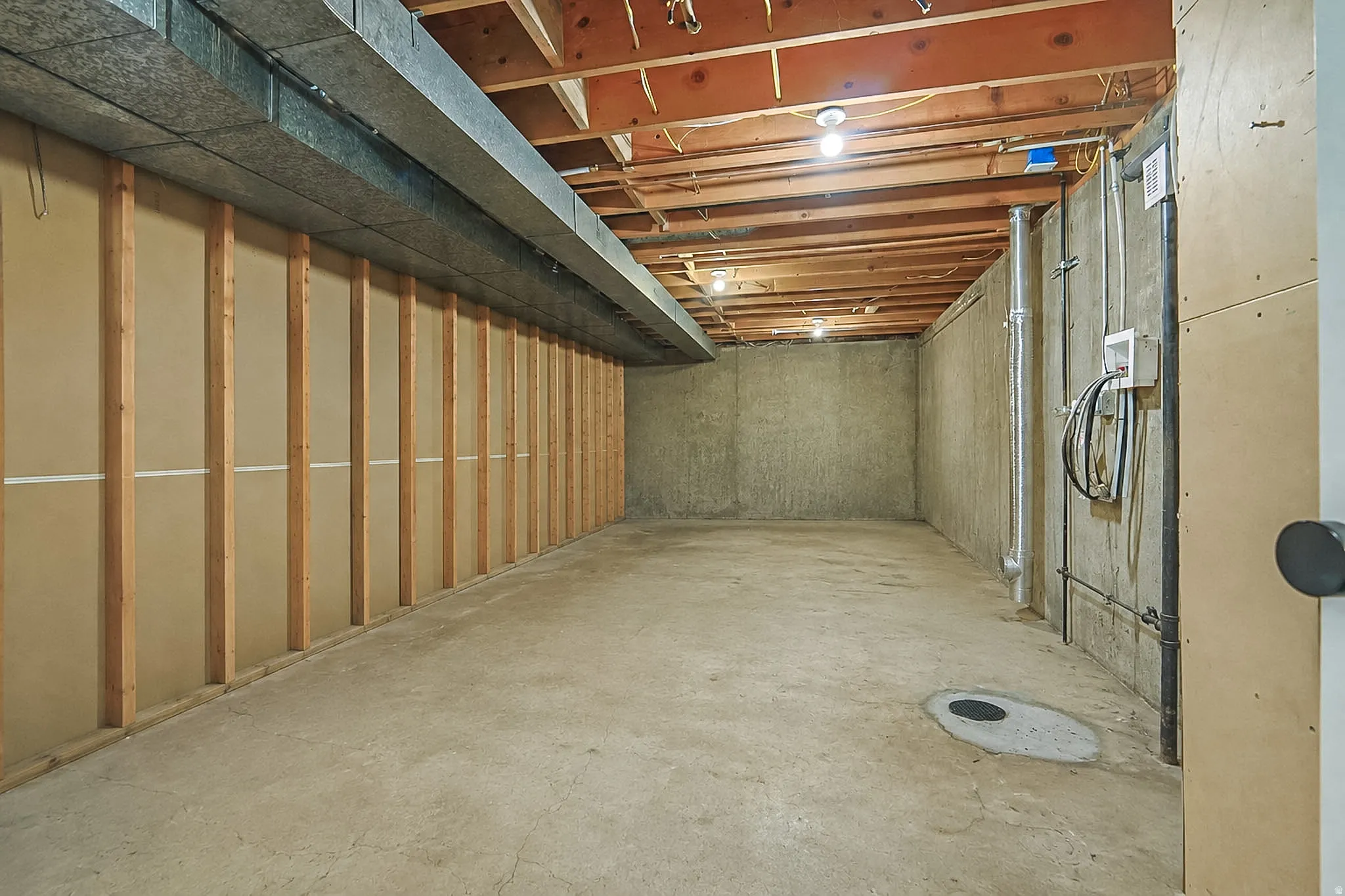 Unfinished basement offering exposed wood joists, concrete flooring, and partial wood-frame wall construction