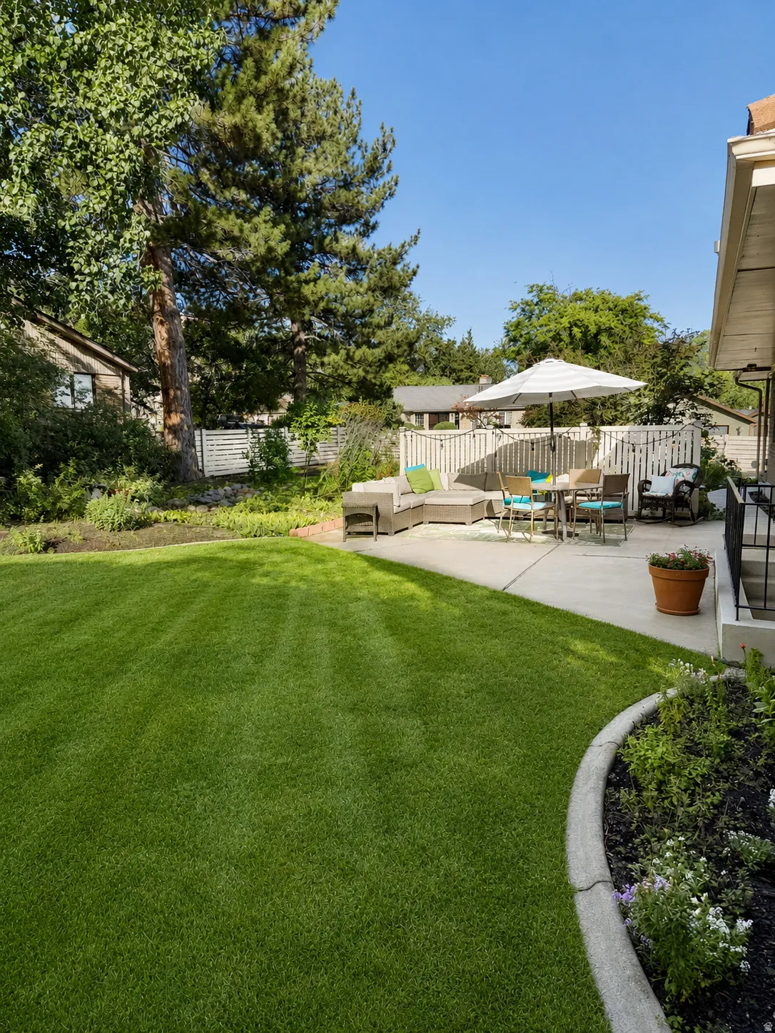 Expansive lawn area with mature trees, concrete patio, and garden beds with curb edging