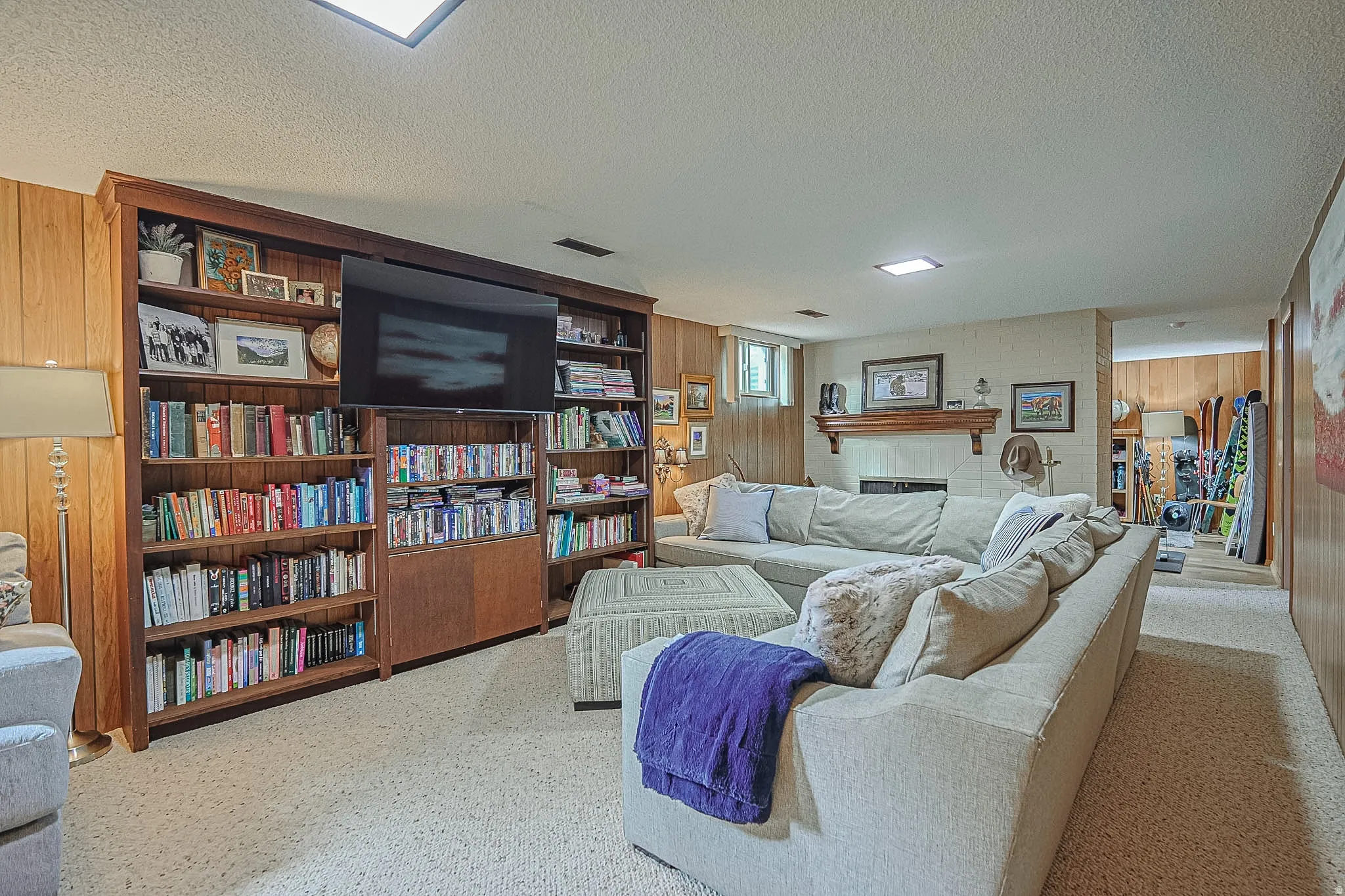 Built-in wood shelving, ceiling lighting, paneled wall accents, carpeted flooring, and a fireplace with wood mantel