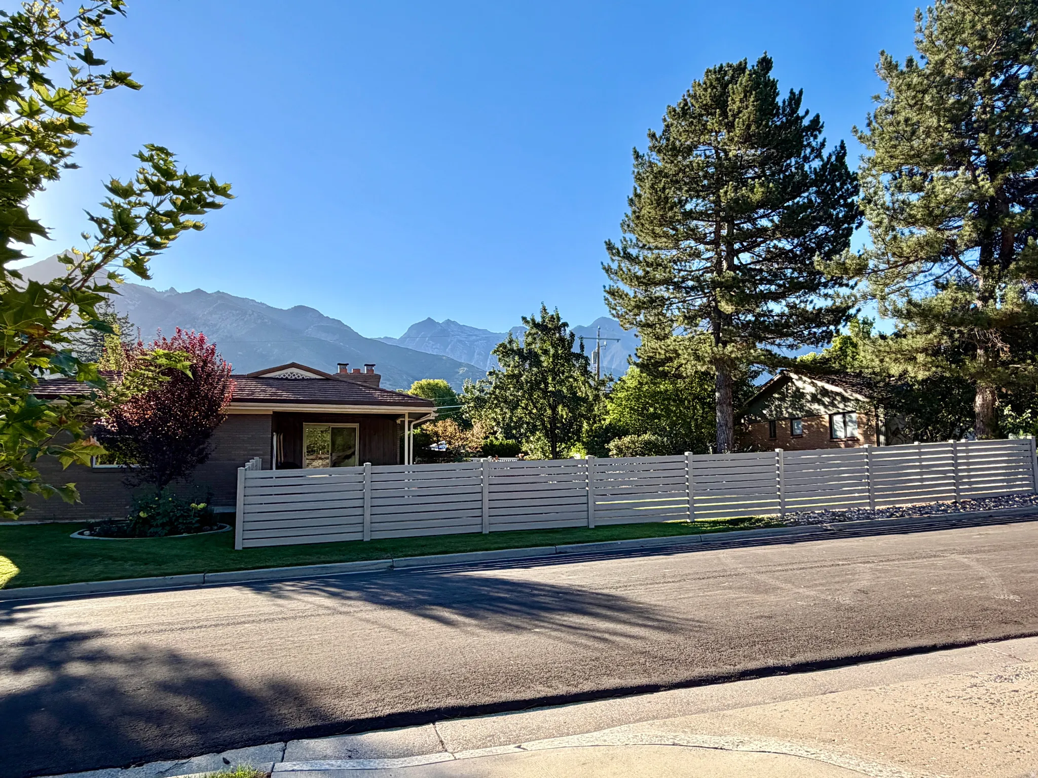 Mountain backdrop, mature trees, horizontal slat fencing, expansive paved street, manicured lawn