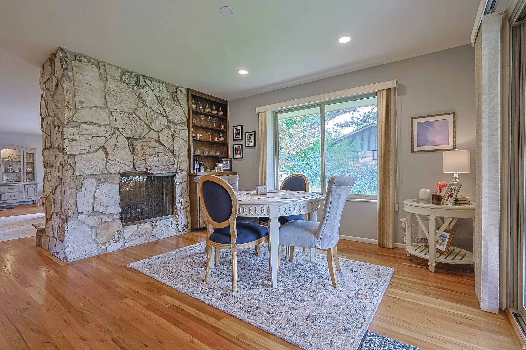 Hardwood flooring, stone fireplace, built-in shelving, large window, and recessed lighting