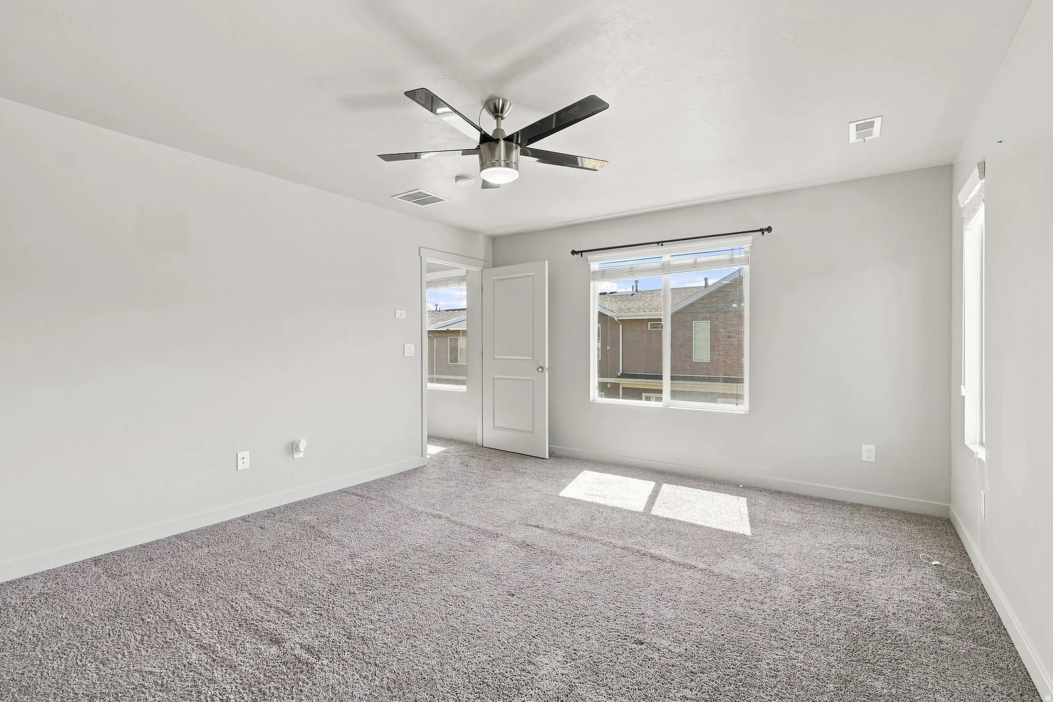Spacious interior with neutral-toned walls, gray carpeting, and a contemporary ceiling fan