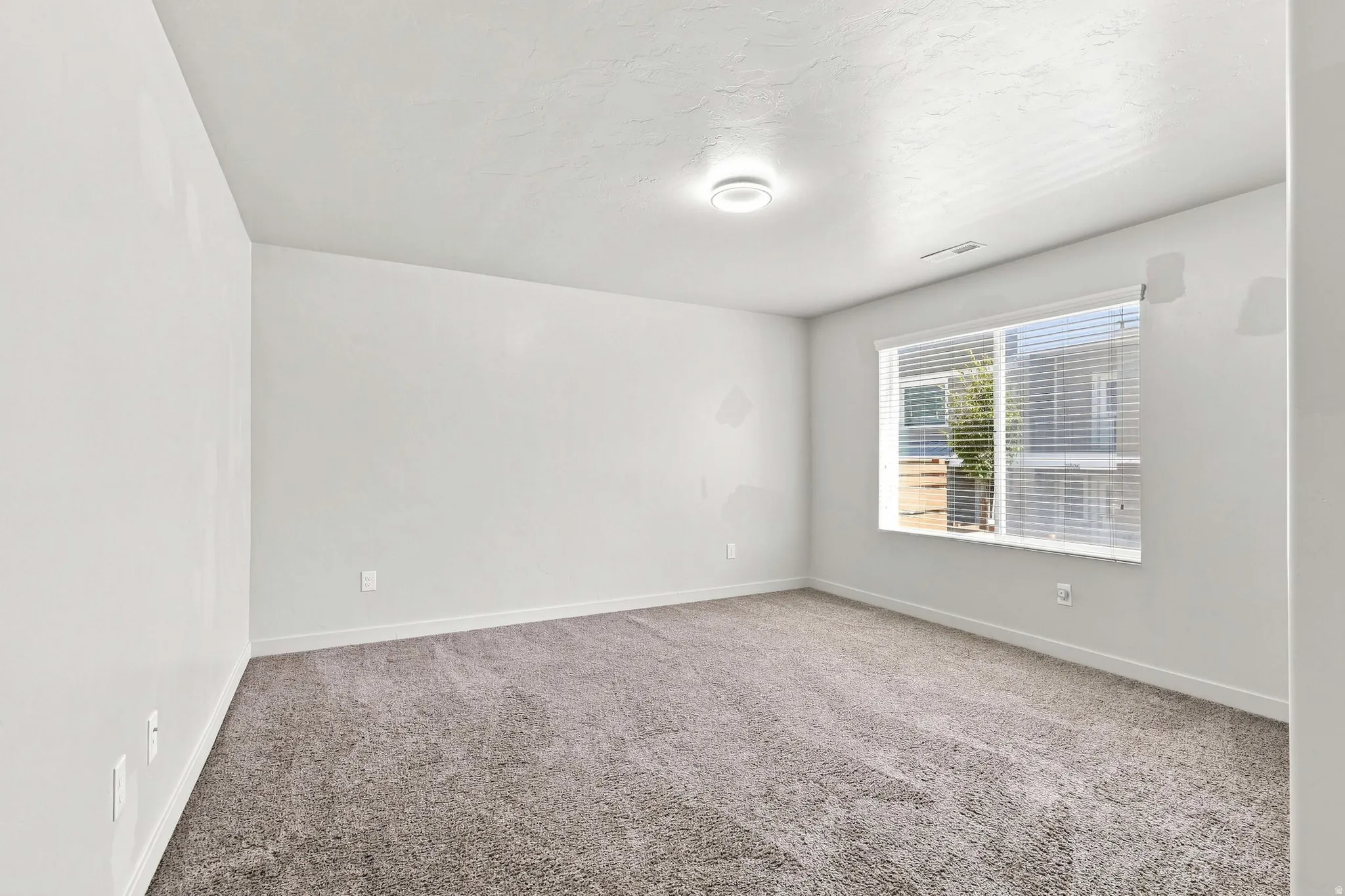Bright secondary bedroom featuring neutral carpeting, recessed ceiling lighting, and large double-hung windows with blinds providing natural illumination and privacy control