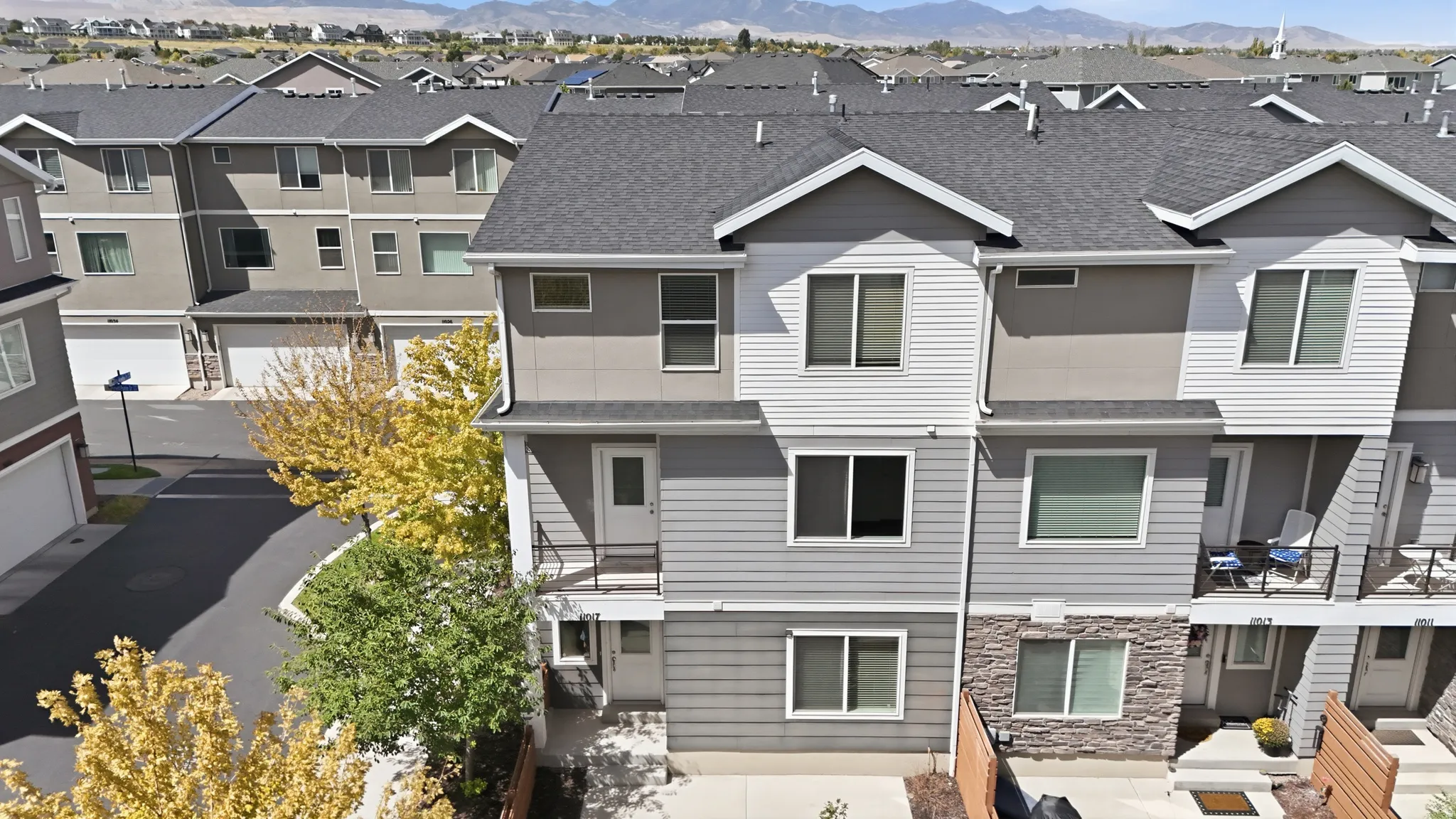 Three-story townhome with a multi-textured exterior, featuring stone accents, horizontal siding, and a dark shingle roof