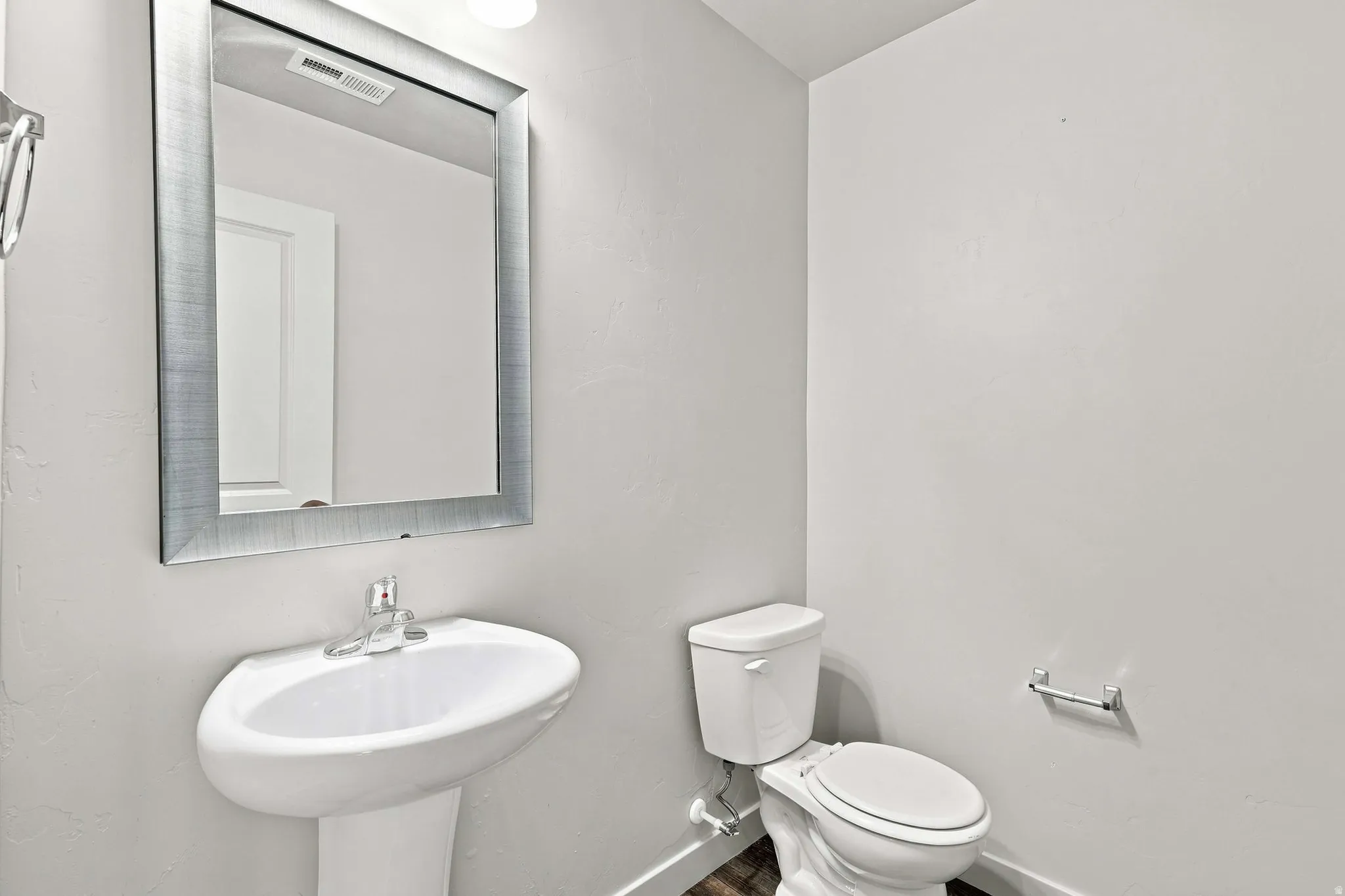 Pedestal sink with chrome faucet, framed wall mirror, and a white toilet