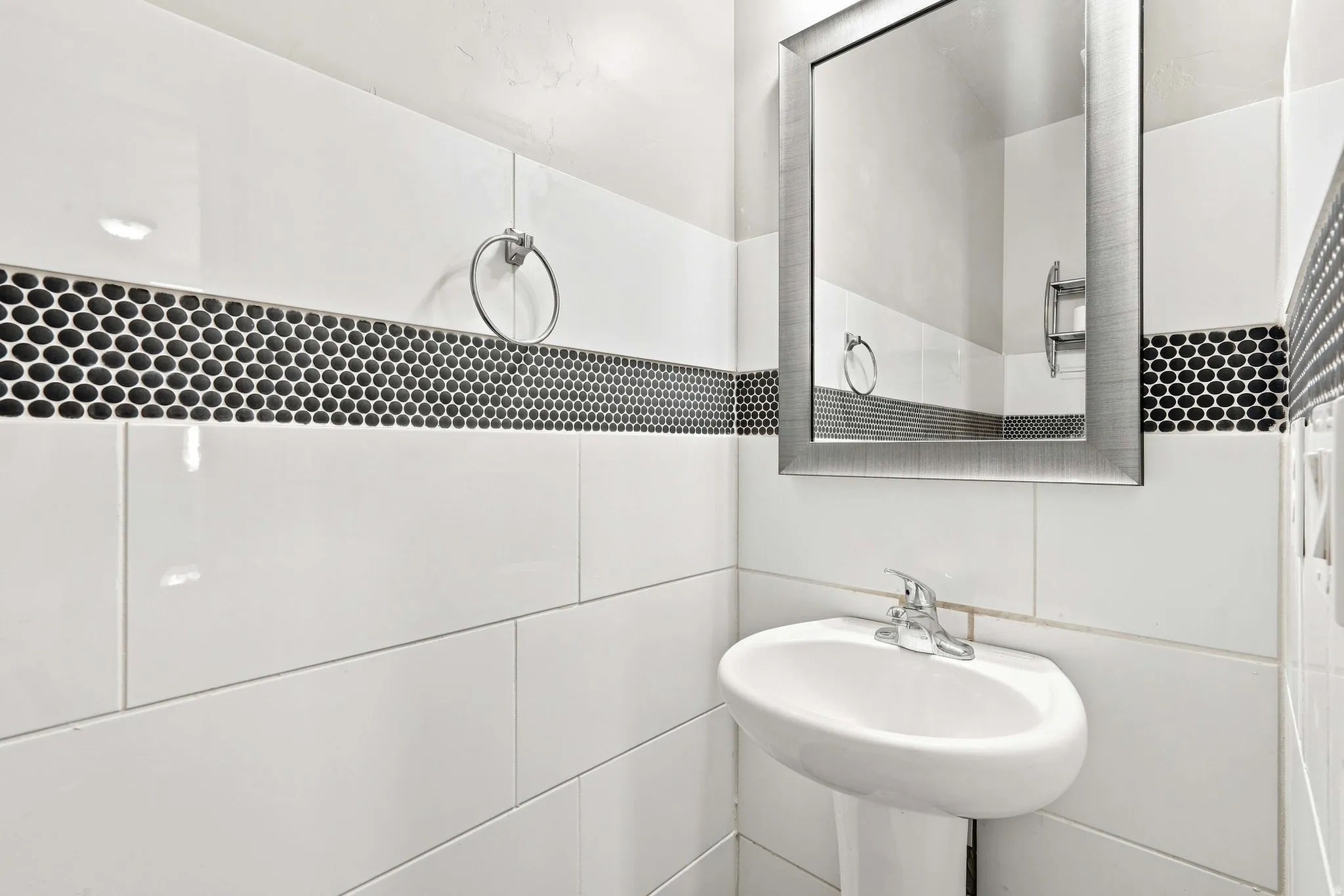 Modern bathroom featuring crisp white subway tile walls, a decorative black hexagonal tile accent band, polished chrome fixtures, a round pedestal sink, and a framed mirror with brushed metal trim