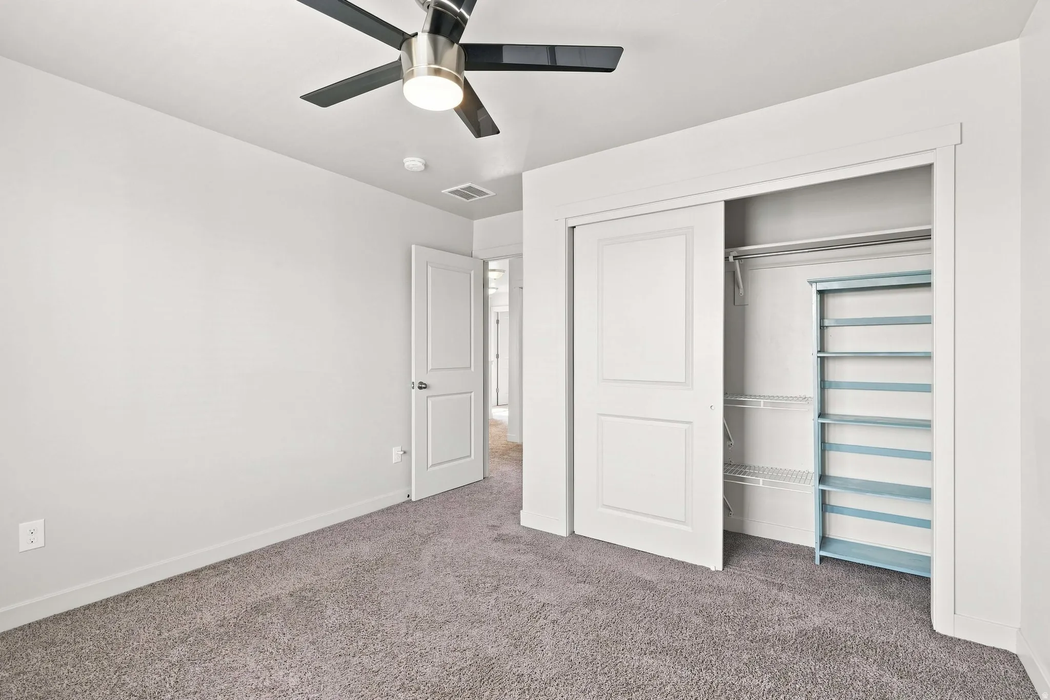 Plush carpet flooring, ceiling fan with integrated lighting, double-panel interior door, and a closet with sliding doors and wire shelving