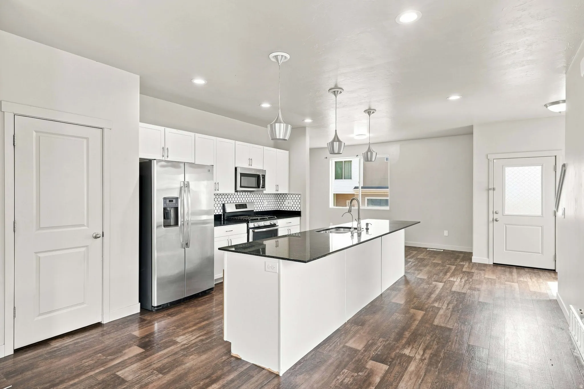 Open-concept kitchen with white cabinetry, stainless steel appliances, a central island with a sink, and wood-finish flooring