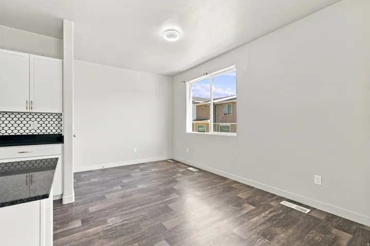 Wood-finish flooring, white cabinetry, dark countertop, patterned tile backsplash, and a window providing natural light