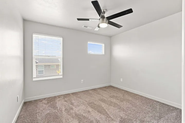 Plush carpeting, contemporary ceiling fan, and two windows providing natural illumination