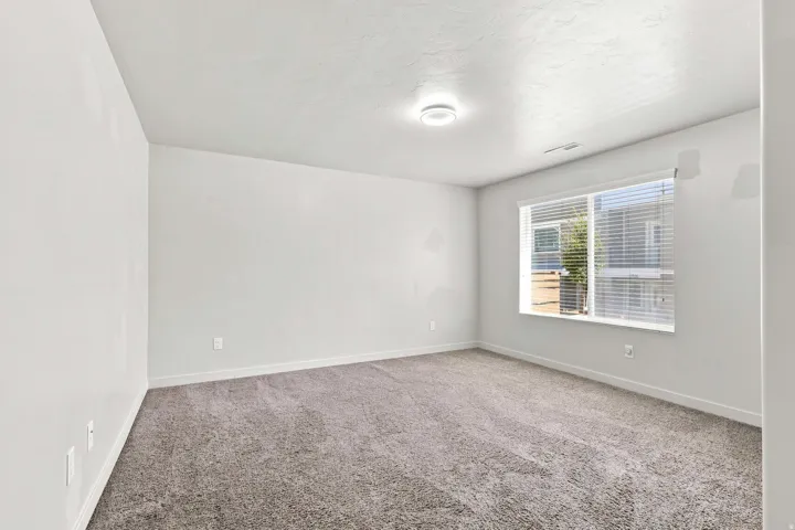 Bright secondary bedroom featuring neutral carpeting, recessed ceiling lighting, and large double-hung windows with blinds providing natural illumination and privacy control