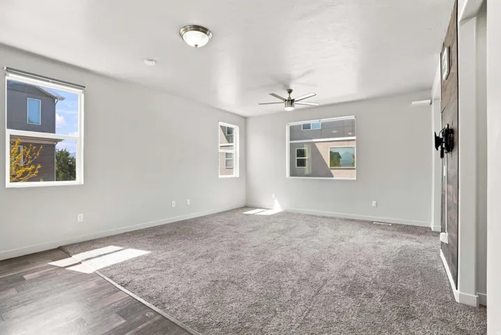 Bright, open living space with abundant natural light from multiple windows, neutral wall finishes, and wood-finish flooring