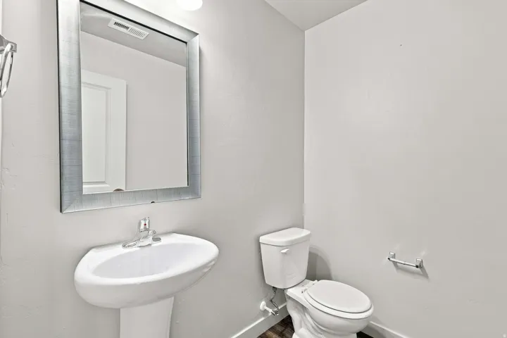 Pedestal sink with chrome faucet, framed wall mirror, and a white toilet