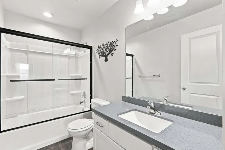 Contemporary bathroom featuring a frameless glass-enclosed shower with black metal trim, dual vanity with gray quartz countertop and rectangular undermount sink, chrome faucet fixtures, and white shaker-style cabinetry