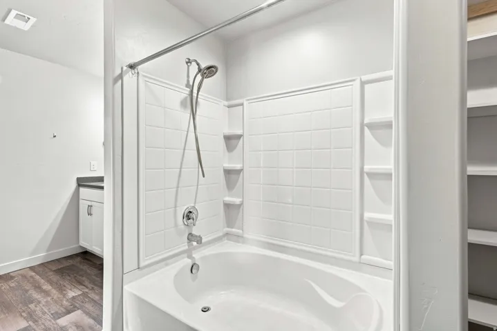 Master bath featuring a white subway tile surround, integrated corner shelving, dual showerheads with handheld spray, and a soaking tub with chrome fixtures