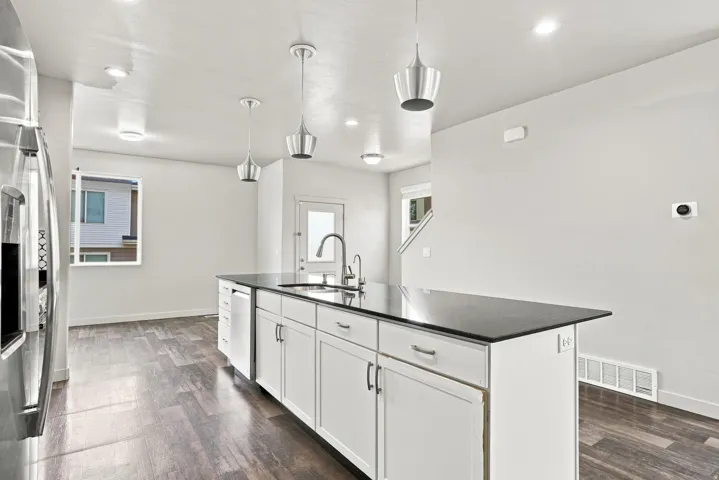 Spacious kitchen island featuring a dark countertop, stainless steel sink with a gooseneck faucet, white cabinetry, and pendant lighting