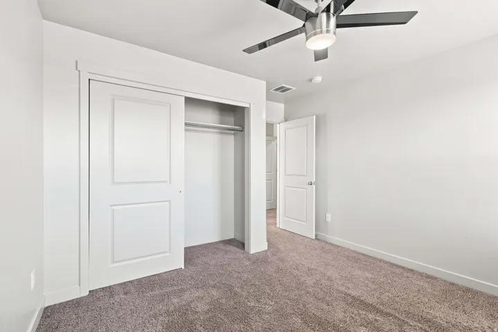 Plush carpeted flooring, a ceiling fan with light fixture, and a built-in closet with sliding panel doors
