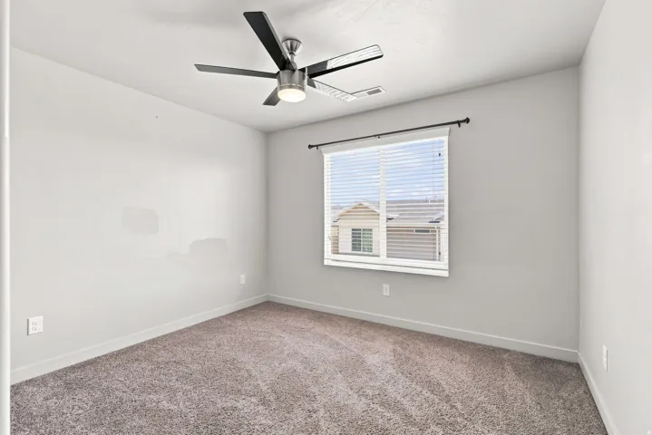 Plush carpeting, neutral wall tones, window with horizontal blinds, and a ceiling fan with integrated lighting