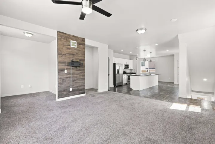 Open-concept living area with gray carpet and wood-finish accent wall