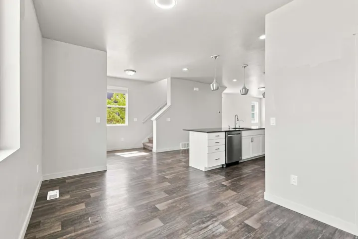 Dark wood-finish flooring throughout, recessed ceiling lighting, kitchen island with dark countertop, stainless steel dishwasher, and contemporary pendant lighting