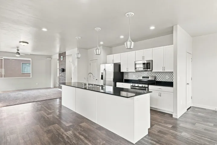 Modern kitchen featuring white cabinetry, black quartz countertops, a large waterfall-edge island, stainless steel appliances, and geometric tile backsplash