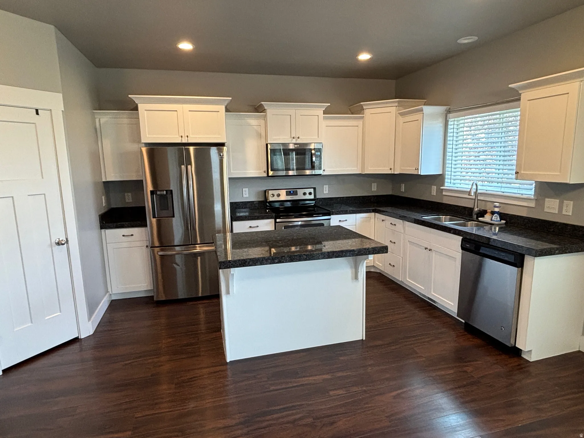 White cabinetry, dark wood-finish flooring, dark stone countertops, stainless steel appliances, and an island with a breakfast bar