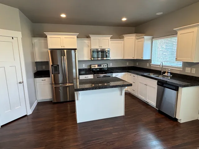 White cabinetry, dark wood-finish flooring, dark stone countertops, stainless steel appliances, and an island with a breakfast bar