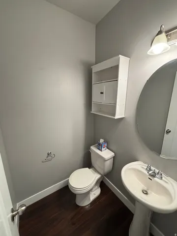 Pedestal sink, wood-finish flooring, wall-mounted storage cabinet, and circular mirror