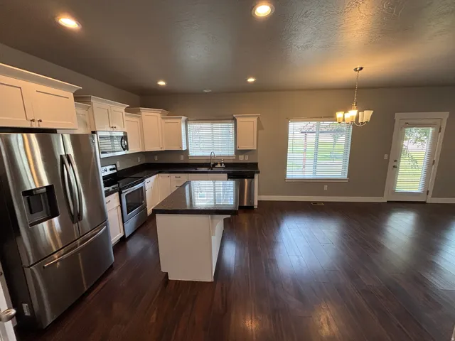 Open concept kitchen and living area with wood-finish flooring, white cabinetry, dark countertops, and stainless steel appliances