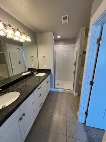 Dual vanity with dark stone countertop, white cabinetry, and overhead sconce lighting