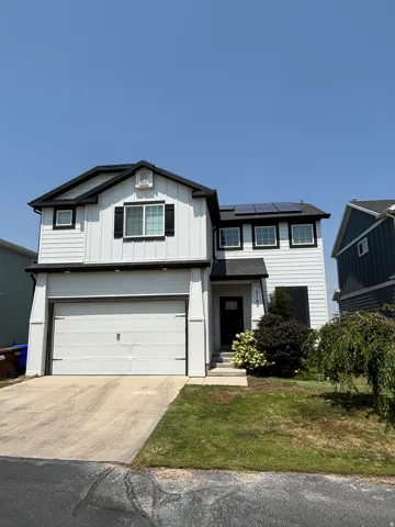 White vertical and horizontal siding, black trim, asphalt shingle roof, attached garage, and solar panels
