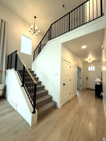 Two-story entry featuring wood-finish flooring, a carpeted staircase with black iron balusters and wood handrail, and an overhead chandelier
