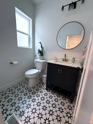 Black and white geometric pattern tile flooring, dark wood-finish vanity with a white countertop, gold-finish faucet, and an oval mirror with a gold-finish frame